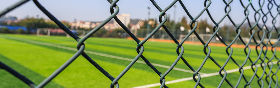 Chain link fencing with outdoor sports facility field in the background.